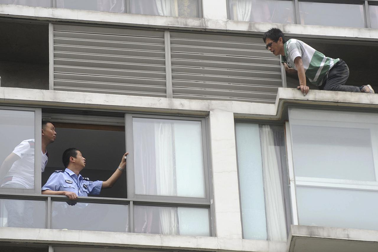 A police officer (2nd L) talks to a man who threatens to jump off the seventh floor of a hotel, in Chengdu, Sichuan province May 19, 2014. The 32-year-old man attempted to commit suicide on Monday after a failed relationship. Police and his ex-girlfriend 
