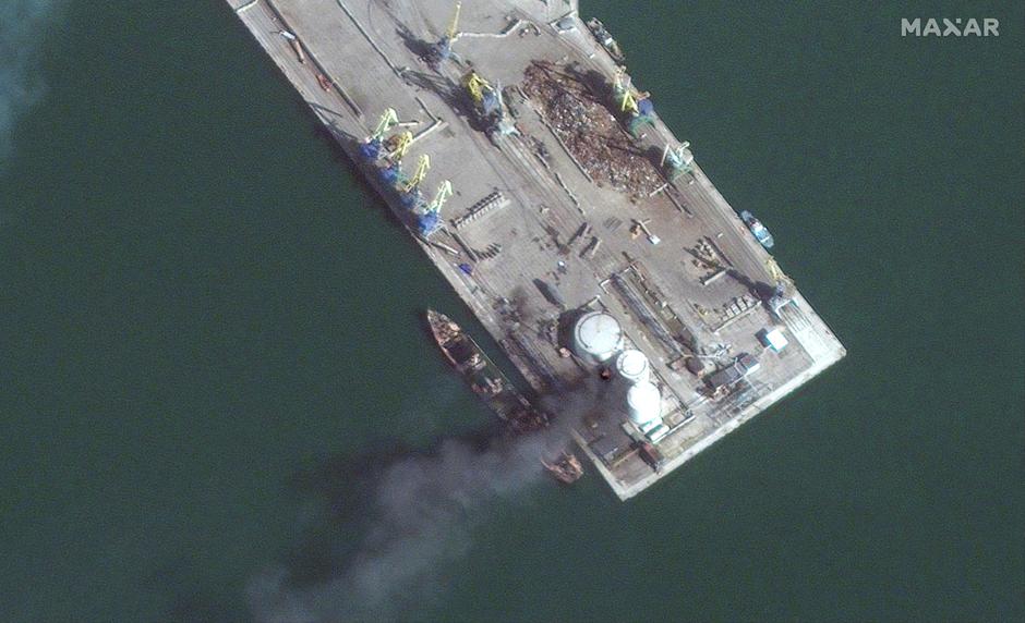 A satellite image shows a burned and partially submerged Russian Alligator-class landing ship and smoke rising nearby, in Berdiansk