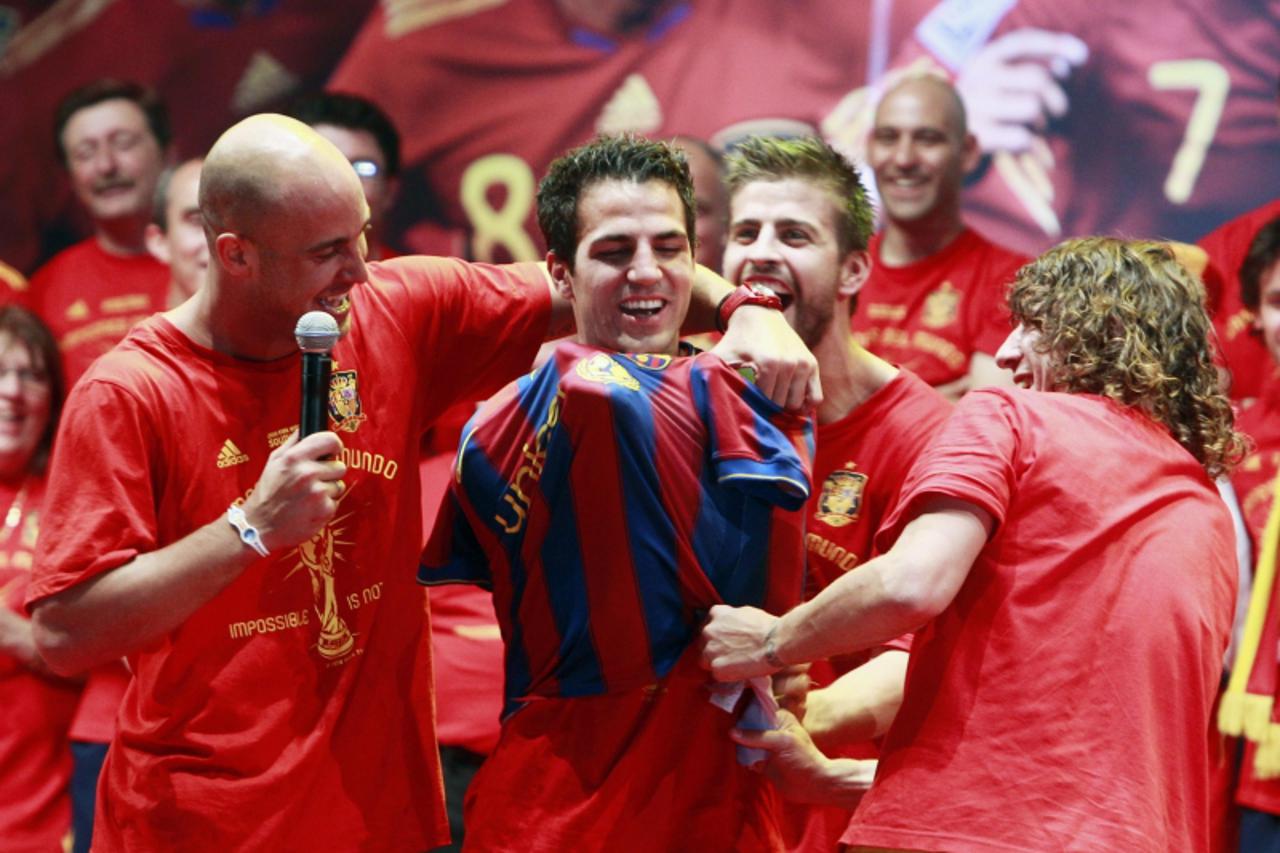 'Spain\'s Pepe Reina and Carles Puyol (R) put a Barcelona shirt on team-mate Cesc Fabregas (C) as they celebrate their victory on a stage in downtown Madrid, July 12, 2010. Spain stunned the Netherlan