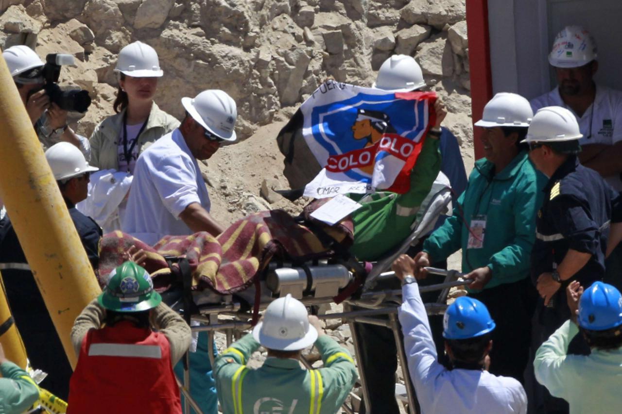 \'Trapped miner Omar Reygadas (C) holds up a flag of the Colo Colo soccer team as he is wheeled to a field hospital after reaching the surface to become the 17th to be rescued from the San Jose mine i