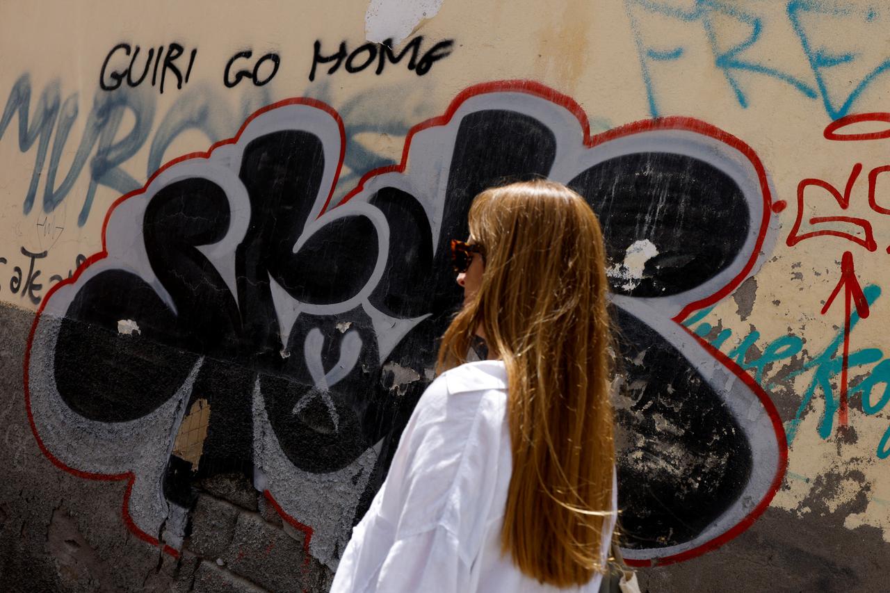 A woman walks past a graffiti on the wall that says "tourist go home" in Las Palmas de Gran Canaria