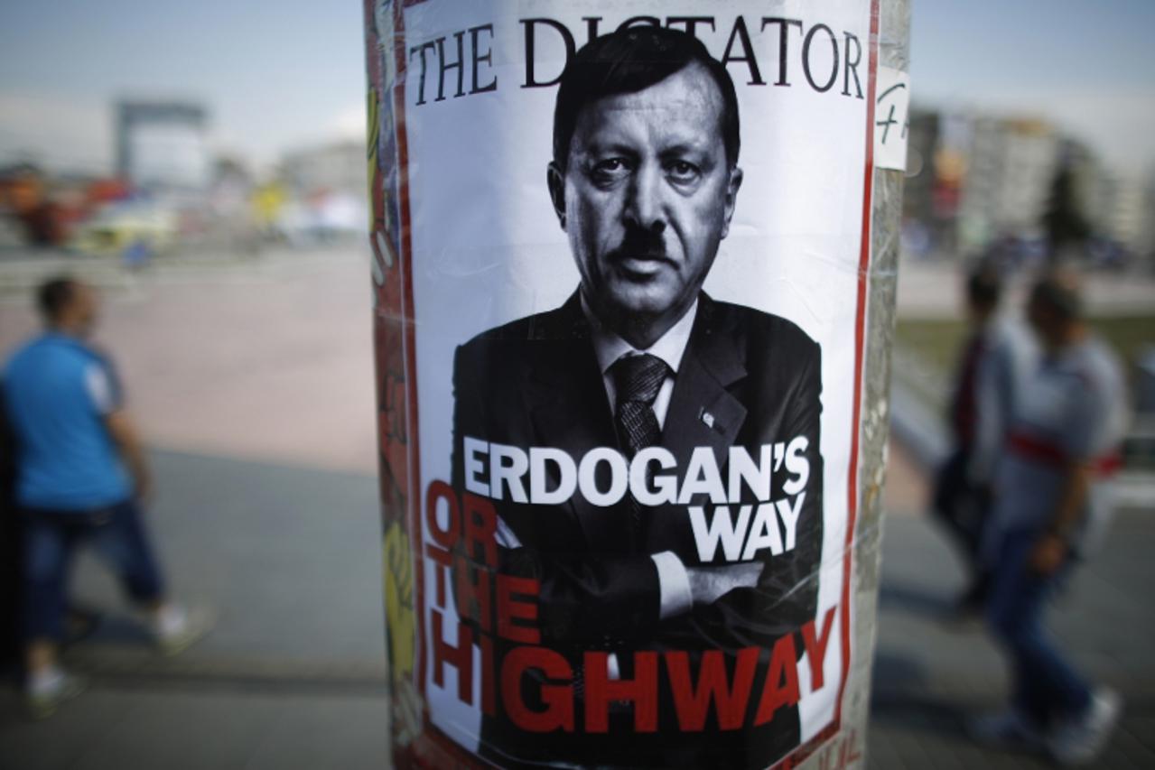 'People walk past a poster depicting Turkish Prime Minister Tayyip Erdogan that has been pasted by demonstrators at Taksim Square in Istanbul June 5, 2013. Protesters clashed with police across Turkey