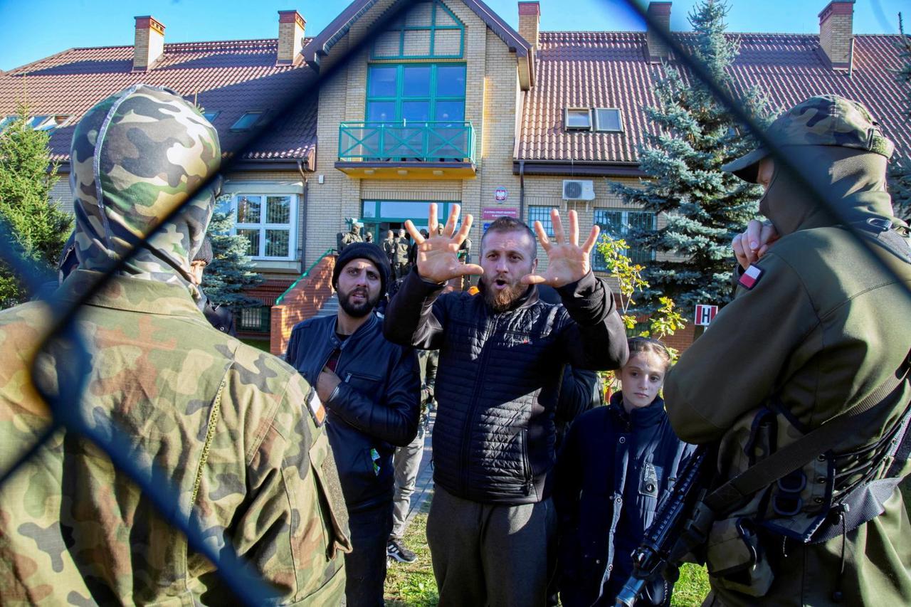 A group of migrants arrested after crossing Polish-Belarus border are held outside the border guard office in Michalowo