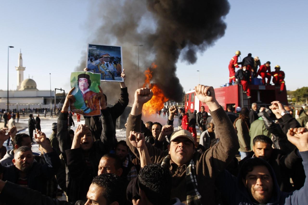 'Men hold up posters of Libya\'s leader Muammar Gaddafi, of which several were distributed among a crowd gathered to view a burning fuel truck, in Tripoli March 2, 2011. Authorities said the incident 