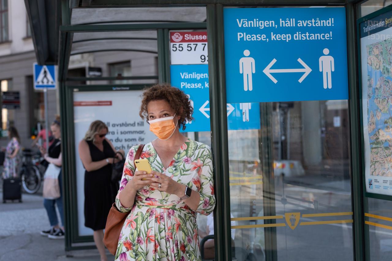 A woman wearing a face mask is seen in a bus stop next to an information sign asking people to keep social distance due to the outbreak of coronavirus disease (COVID-19), in Stockholm