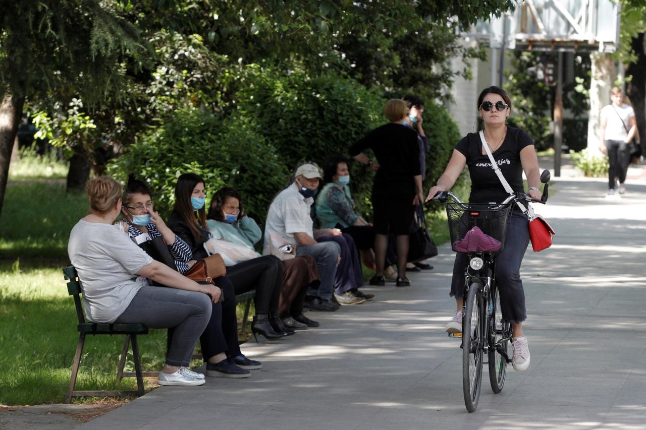 A women rides a bicycle next to people waiting for a bus after Prime Minister Dusko Markovic declared the country the coronavirus disease (COVID-19)-free in Podgorica