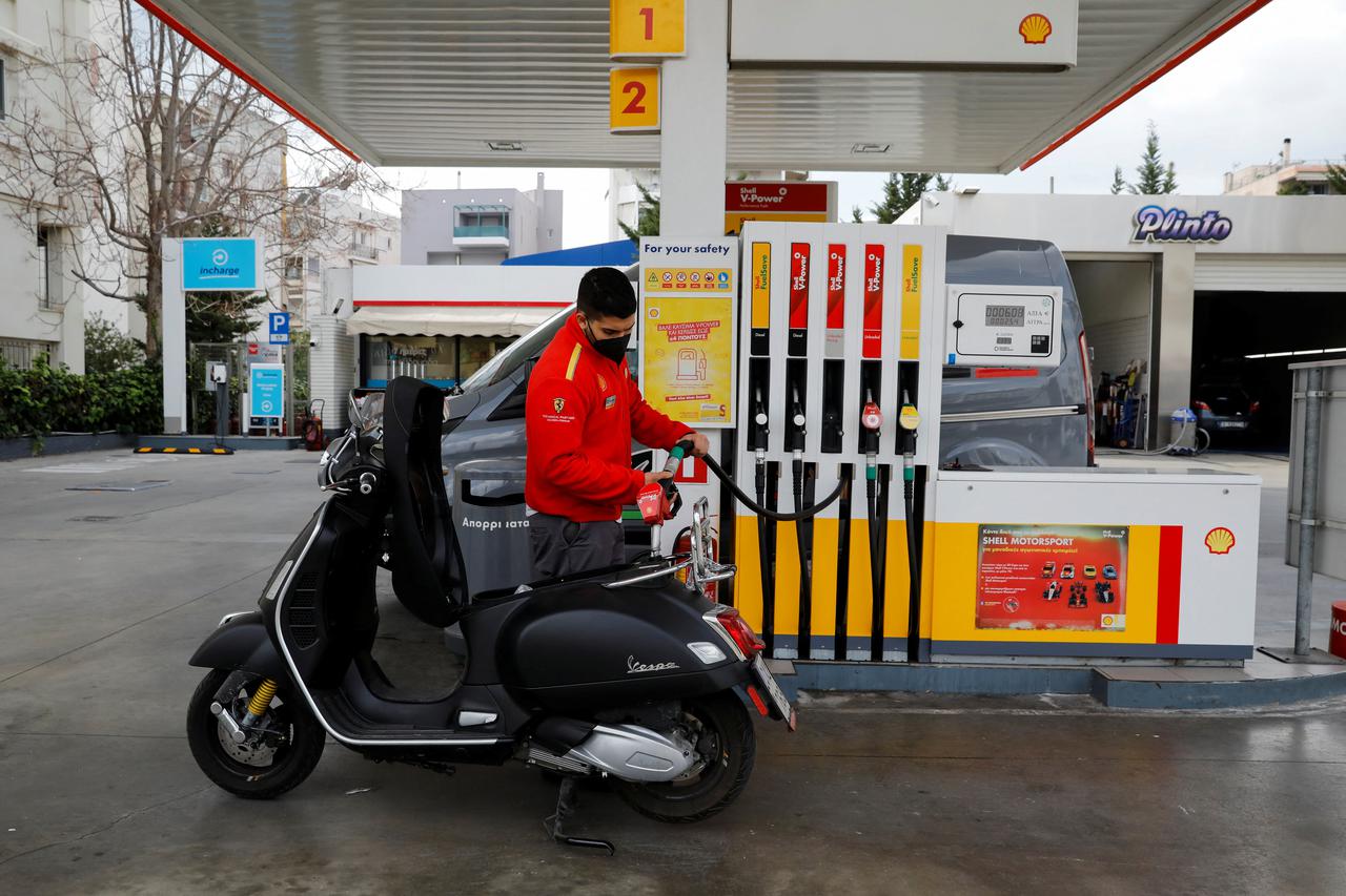 A worker fills a Vespa scooter at a gas station in Athens