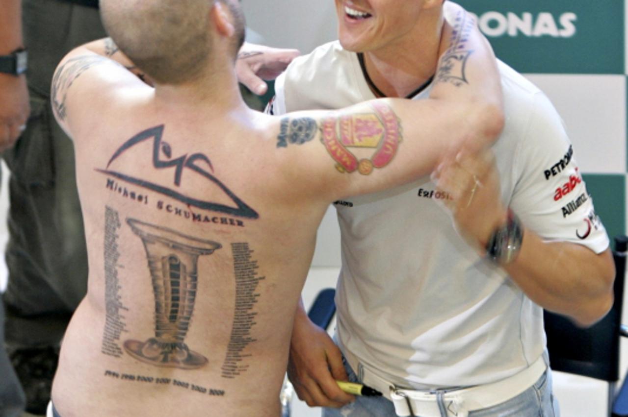 'A tattooed fan hugs Mercedes Formula One driver Michael Schumacher of Germany (R) during a meet the fans session ahead of the Malaysian F1 Grand Prix, in Kuala Lumpur April 6, 2011.  REUTERS/Samsul S