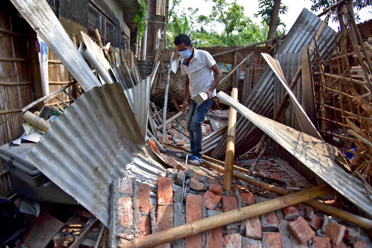 A man searches for his belongings amidst the debris after a boundary wall of his house collapsed following an earthquake in Nagaon