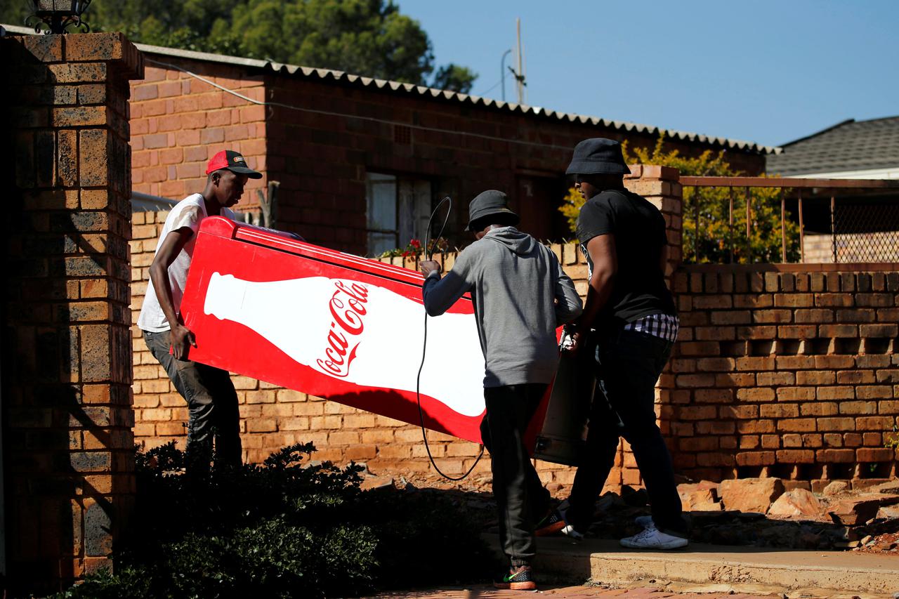 Locals carry a Cocacola branded refrigerator they looted at a nearby shop during protests in Atteridgeville, a township located to the west of Pretoria Locals carry a Cocacola branded refrigerator they looted at a nearby shop during protests in Atteridgev