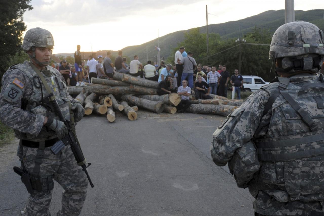 \'U.S. NATO soldiers look at Kosovo Serbs sitting on the road blockade in the village of Zupce near Mitrovica July 28, 2011. NATO said it had declared two crossings on Kosovo\'s border with Serbia a r