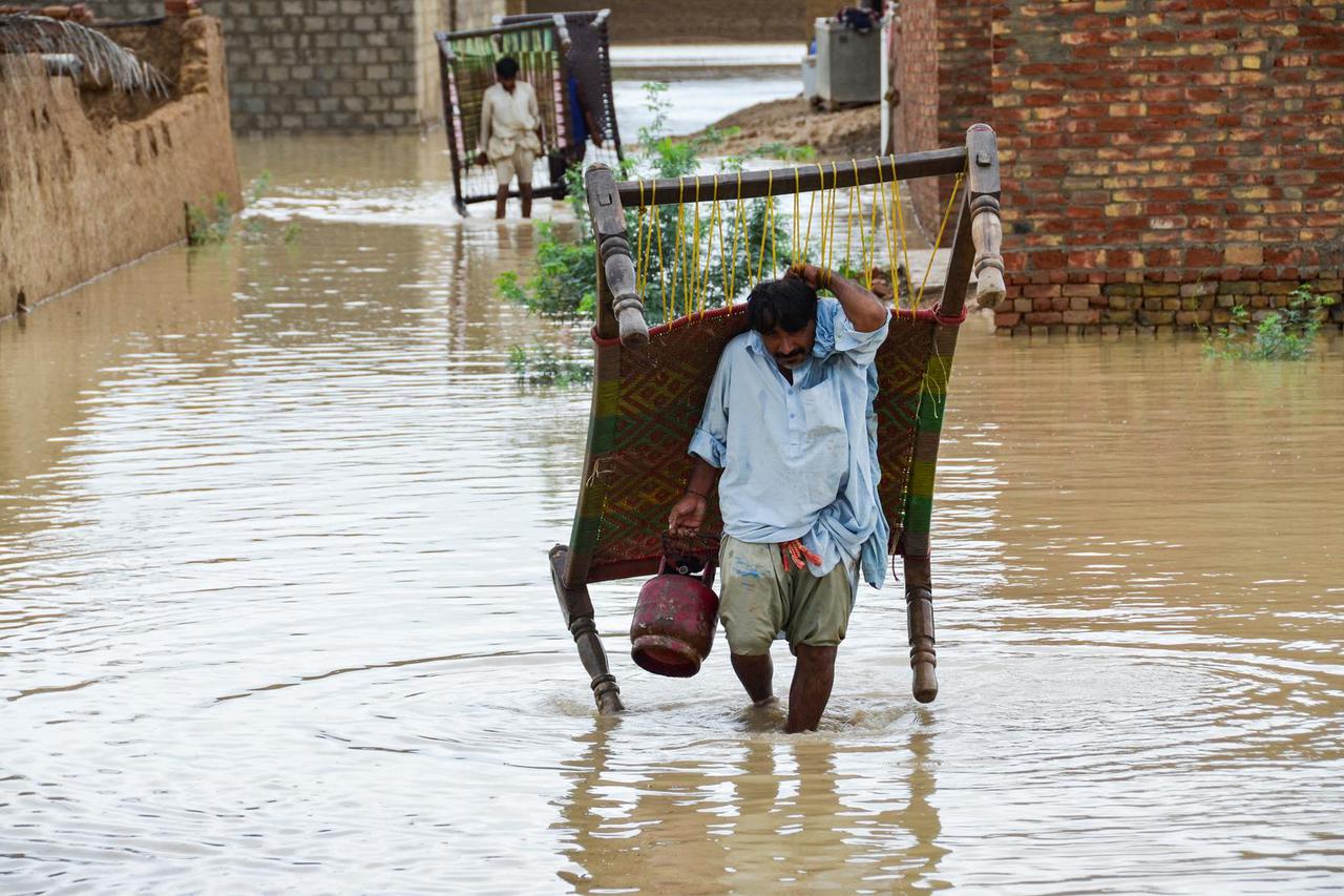 Men walk with their belongings through rain waters following rains and floods during the monsoon season in Dera Allah Yar