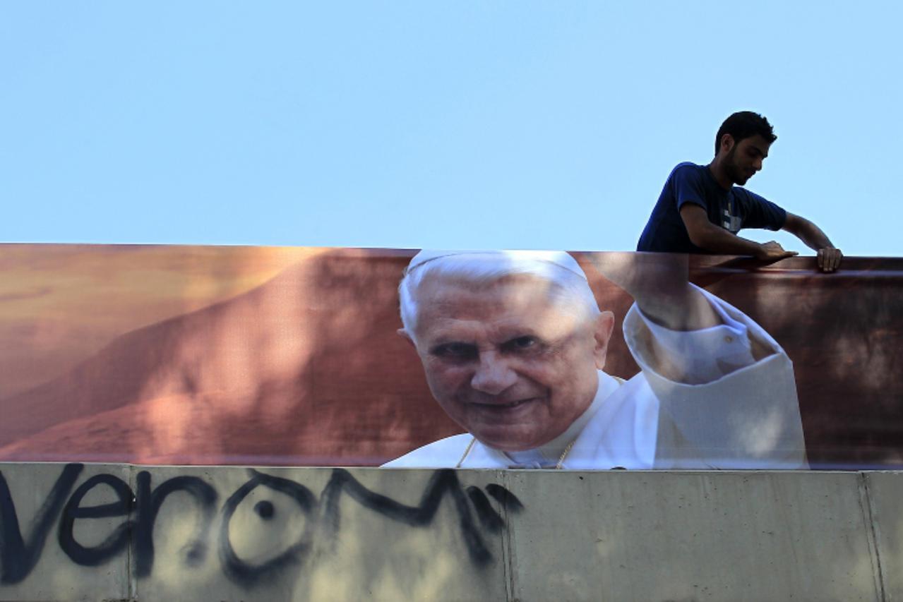 'A worker hangs a banner bearing the picture of Pope Benedict XVI in Dora, north Beirut, on September 6, 2012 ahead of the pope's visit on September 14-16. Security forces have been placed on alert a