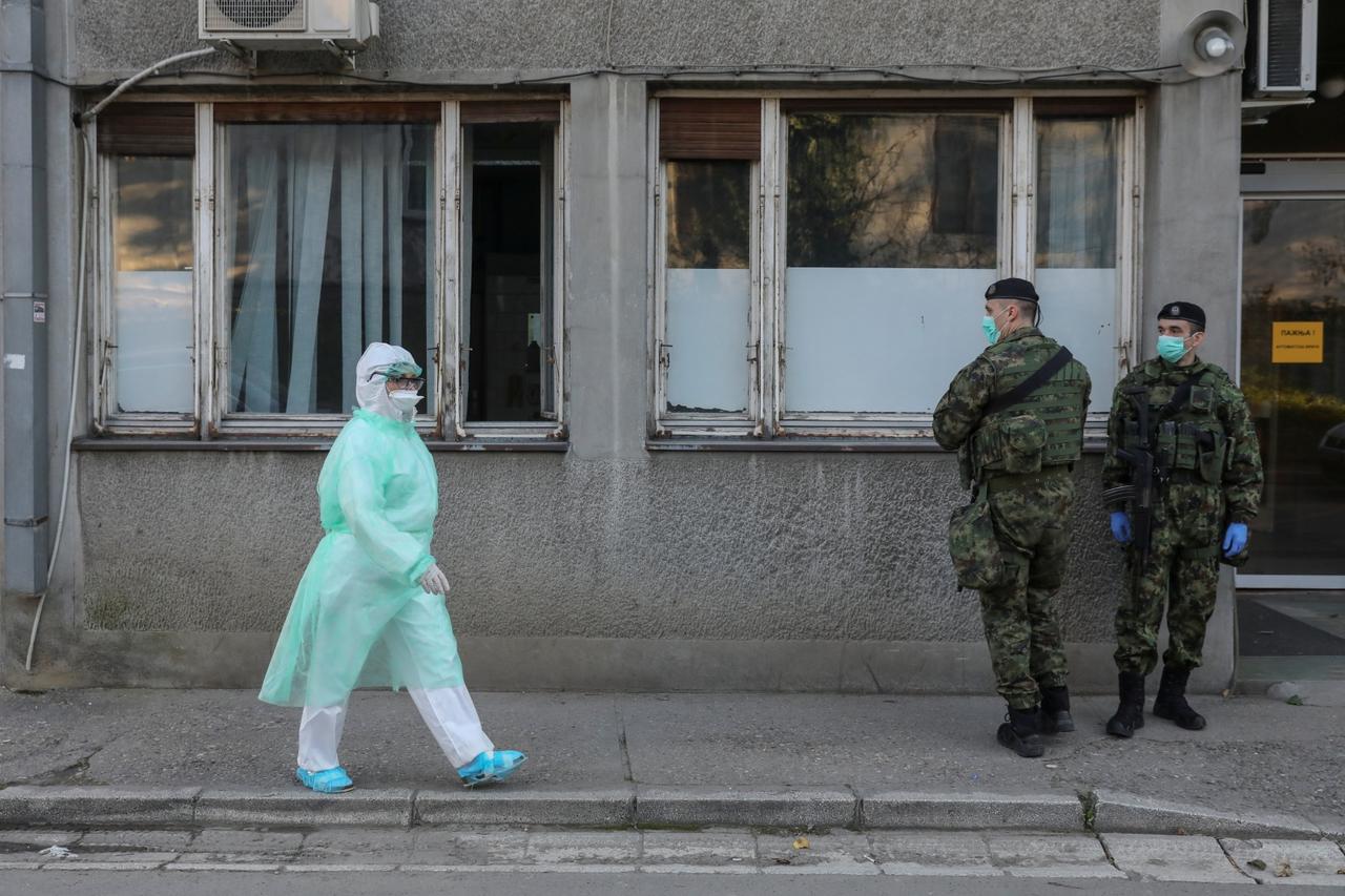 A medical worker walks past Serbian army soldiers in front of the infection clinic as the number of coronavirus (COVID-19) cases grow around the world in Belgrade