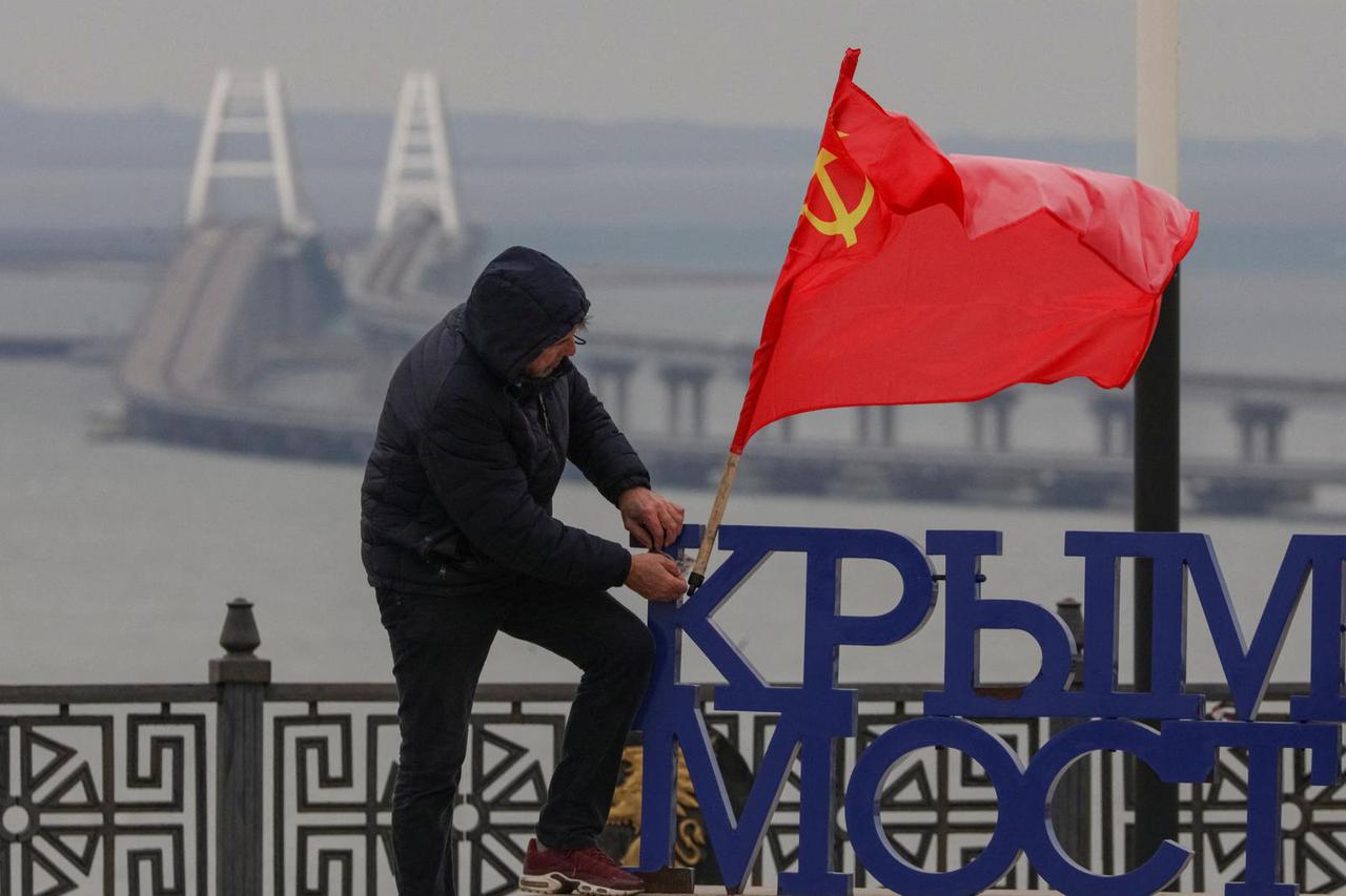 A man puts a Soviet flag at an observation point, with backdrop of the Crimea bridge in the Kerch Strait