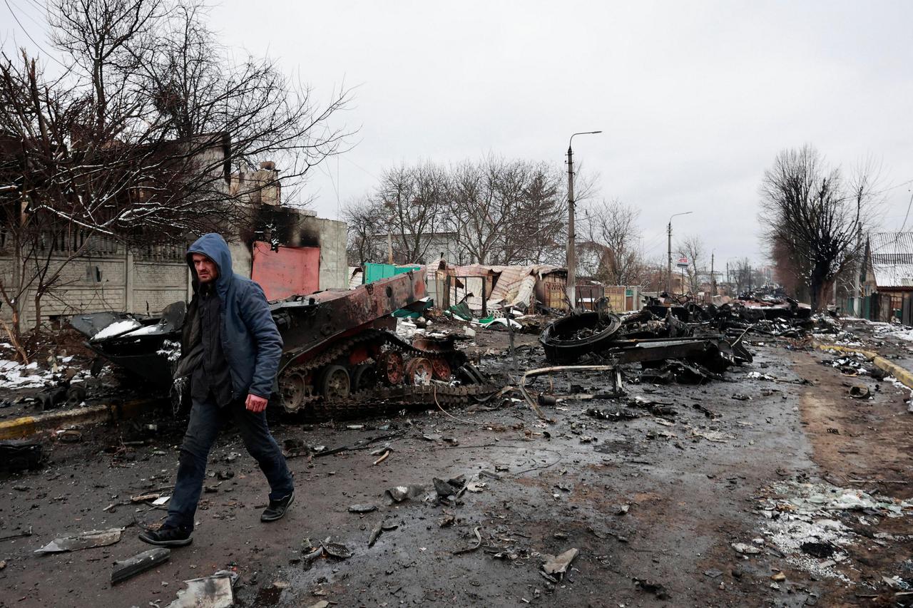 A man walks past destroyed military vehicles on a street in Bucha