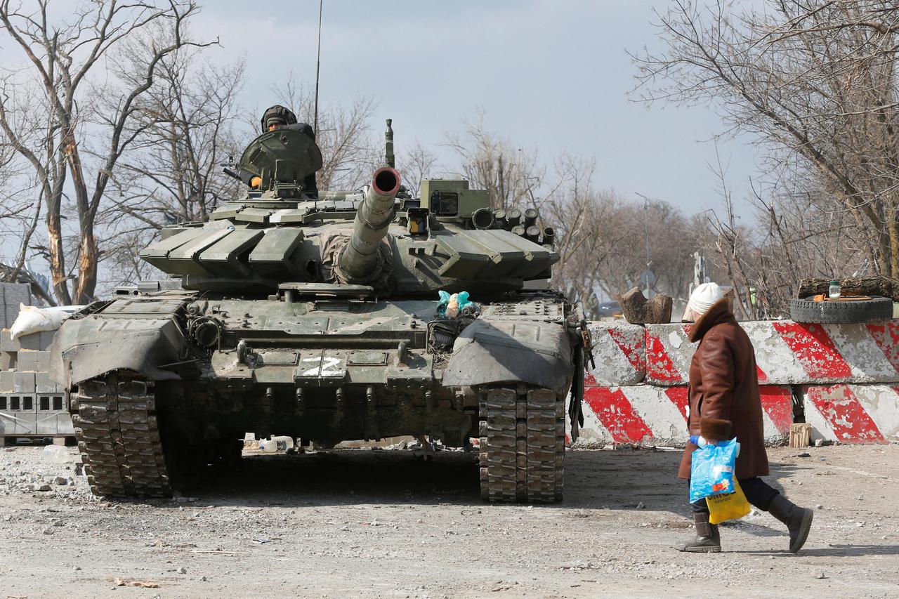 A local resident walks past a tank of pro-Russian troops in the besieged city of Mariupol