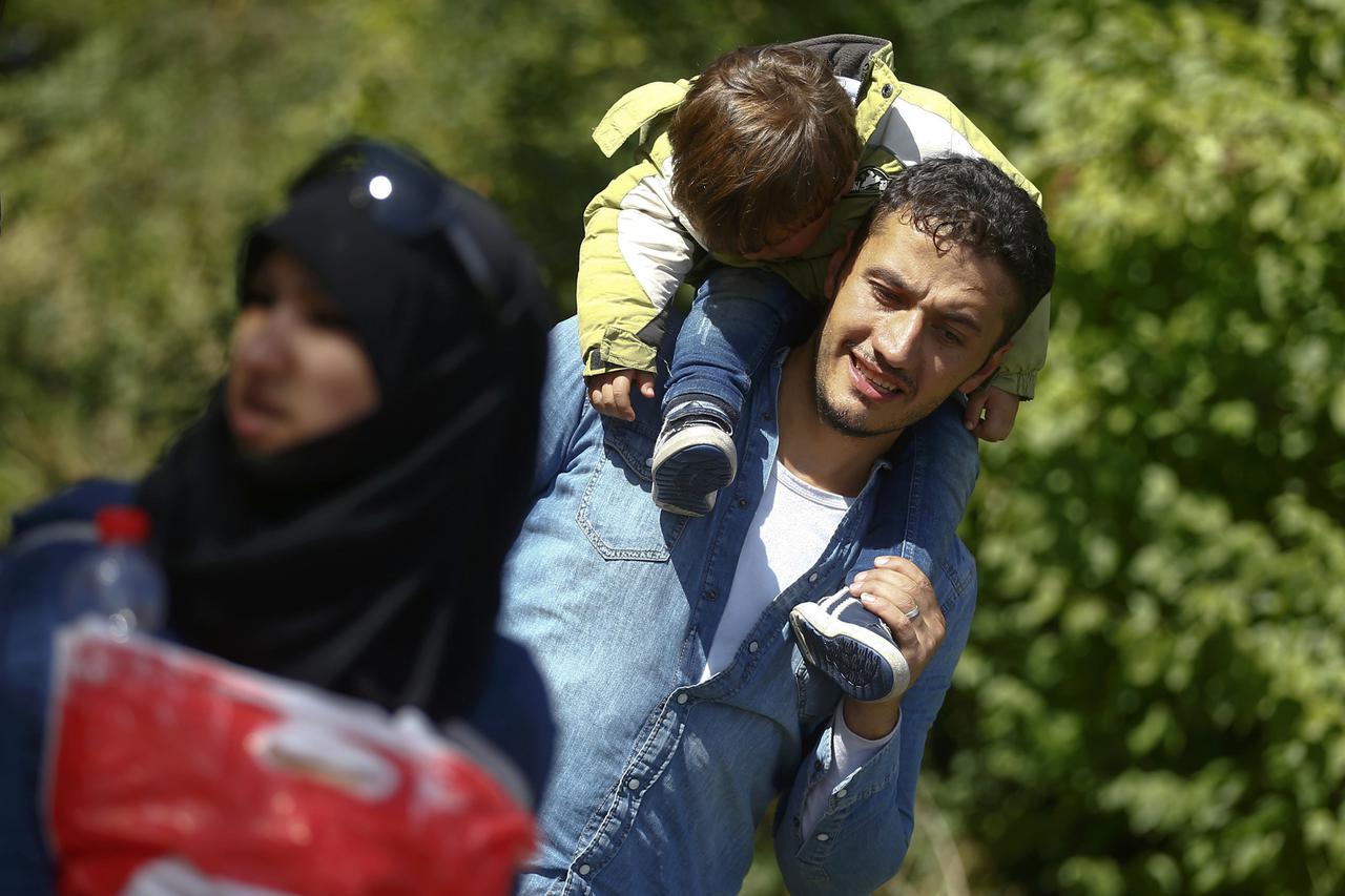 A migrant carries a child as they cross on foot the border from Austria to Freilassing, Germany September 16, 2015. Germany cut its train link with the Austrian city of Salzburg on Wednesday, shutting down the main route into its territory for tens of tho