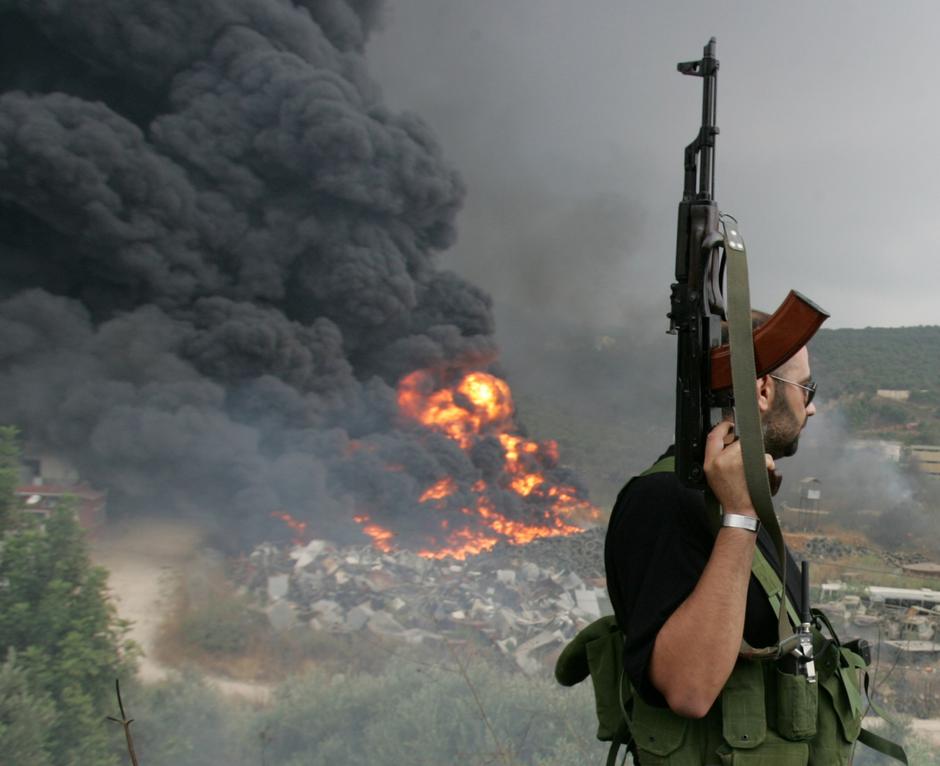 FILE PHOTO: A Lebanese Hezbollah guerrilla looks at a fire rising from a burning object in a Beirut suburb