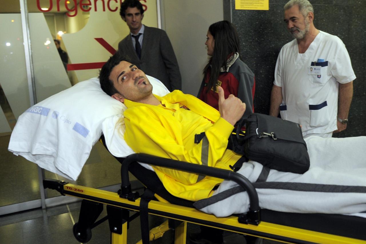 'Barcelona\'s forward David Villa pushed on a gurney at the Quiron Clinic in Barcelona after his arrival from Japan on December 16, 2011. Villa faces up to five months out of the game after breaking h