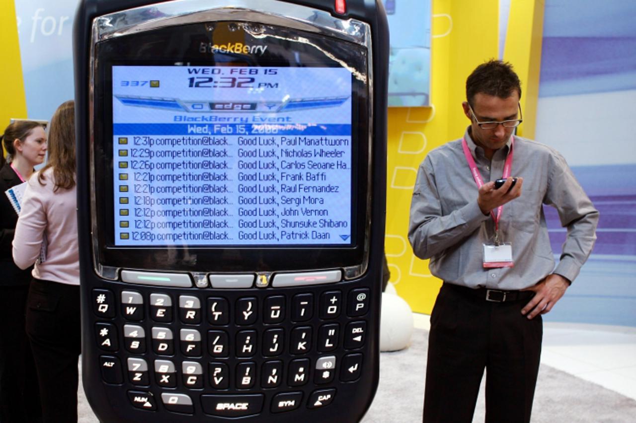 'A visitor looks at a phone as he stands next to a display of the new BlackBerry 8700 at 3GSM World Congress in Barcelona, Spain February 15, 2006. The 3GSM World Congress, which is attended by every 