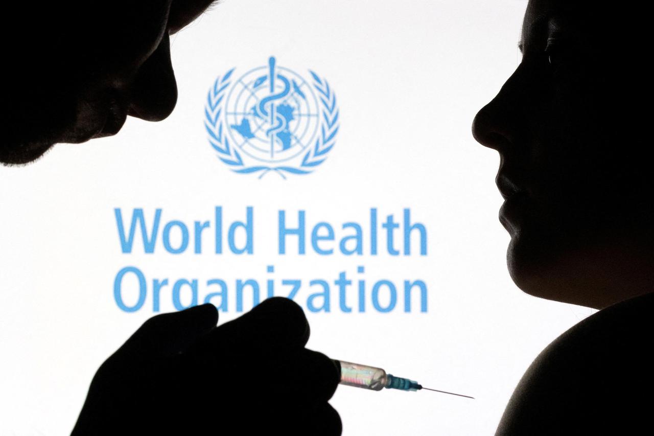 FILE PHOTO: People pose with syringe and needle in front of displayed WHO logo