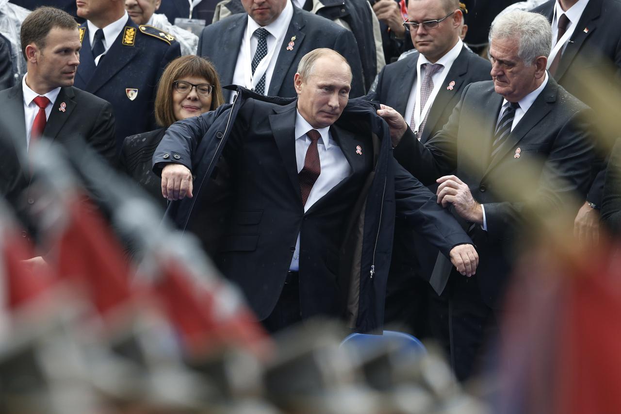 Serbian President Tomislav Nikolic (R) helps Russian President Vladimir Putin (C) with his jacket during a military parade to mark 70 years since the city's liberation by the Red Army in Belgrade October 16, 2014. Serbia feted Russia's Putin with troops, 