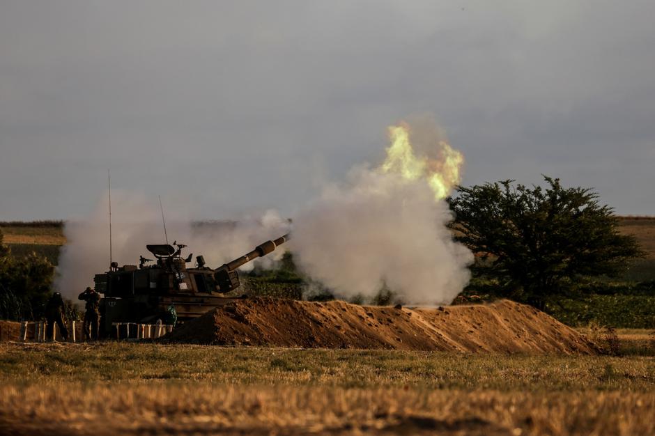 Israeli soldiers stand by an artillery unit as it fires near the border between Israel and the Gaza strip, on the Israeli side