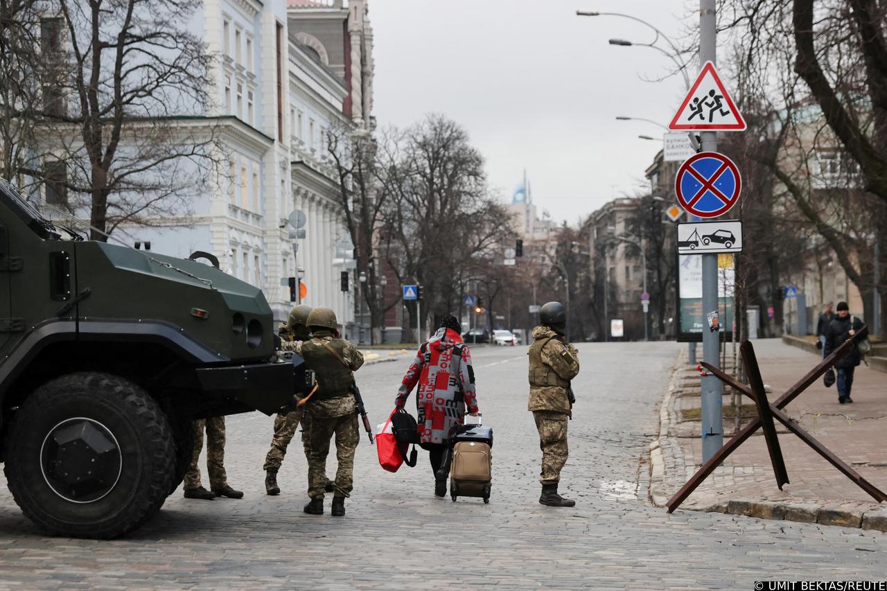 A woman walks past Ukrainian military service members guarding a road in Kyiv