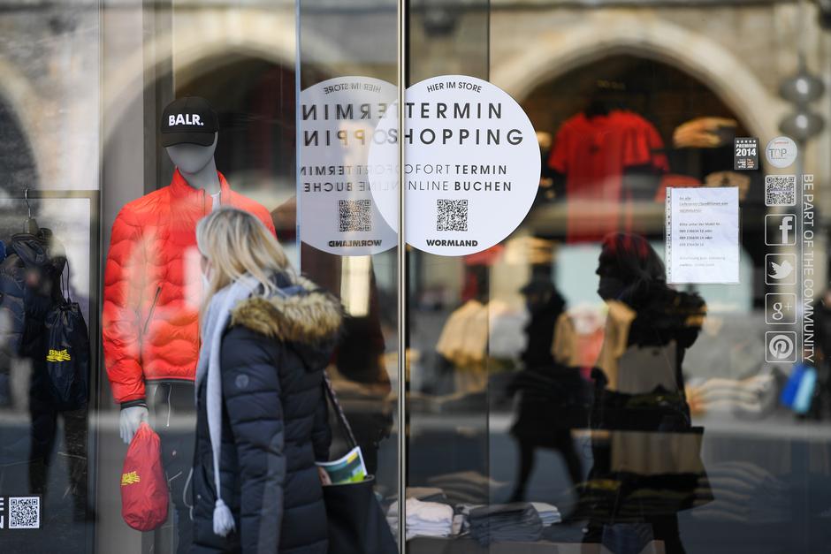 A woman passes a shop with a sticker reading "shopping by appointment" in the city center in Munich