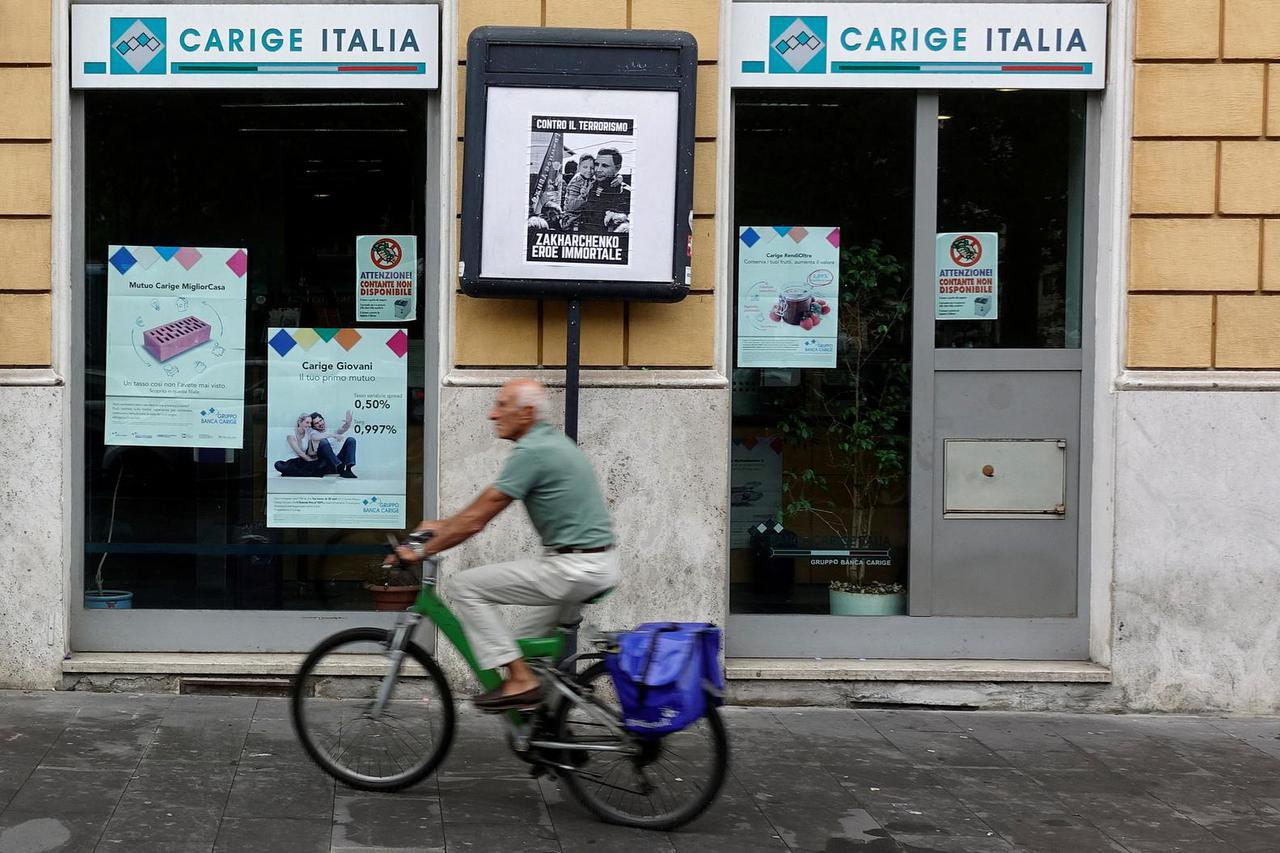 FILE PHOTO: A man rides a bicycle past a Carige bank in Rome