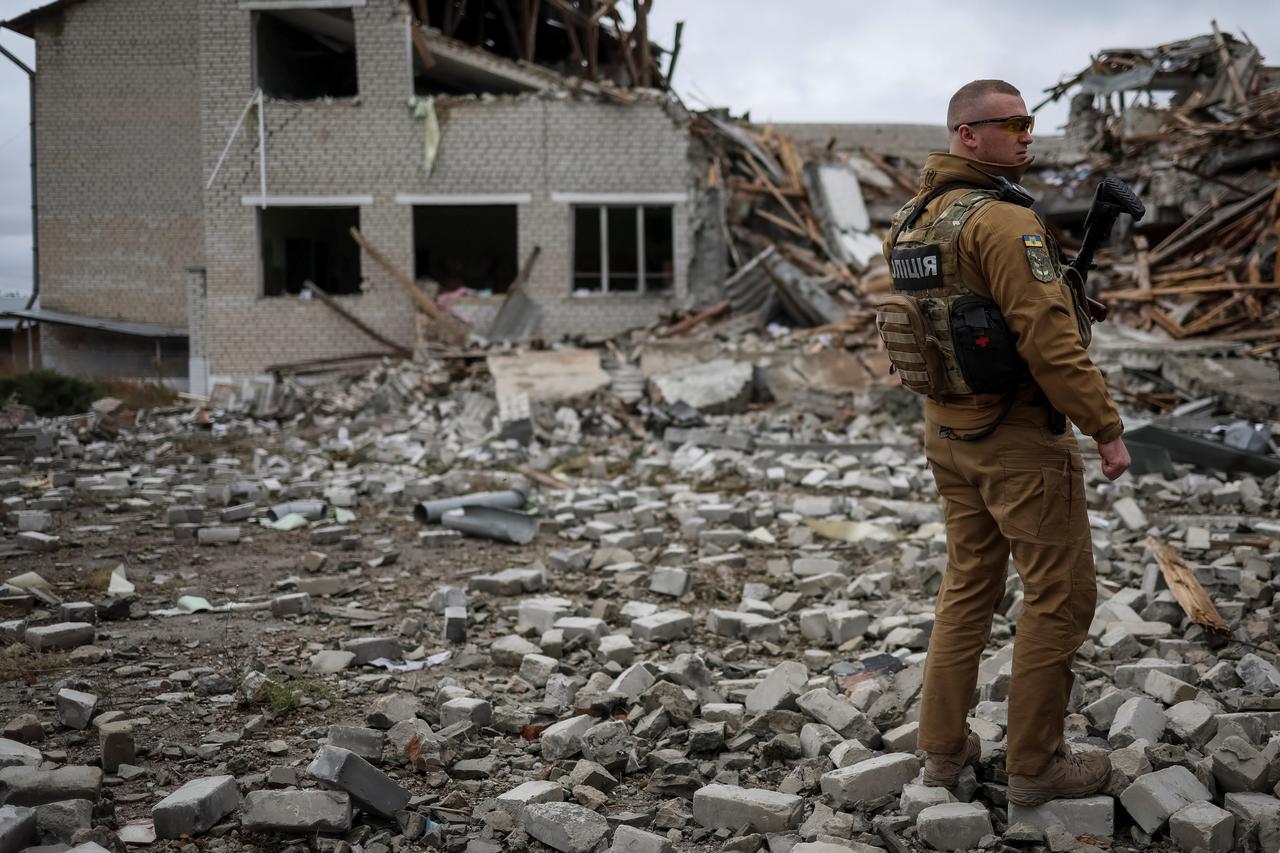 Ukrainian police officer stands guard near destroyed school building, in the village of Verbivka