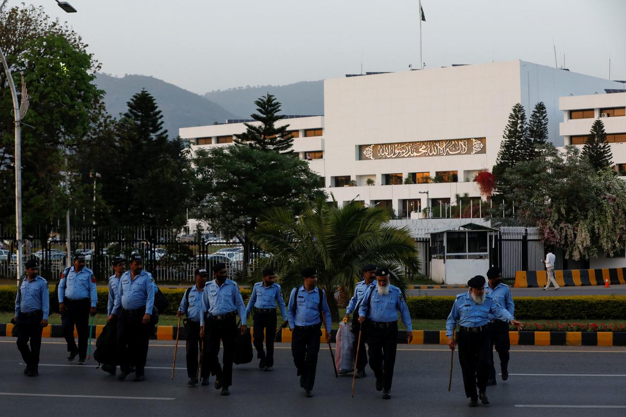 Police officers walk to cross road, with the Pakistan's parliament building in the background, in Islamabad