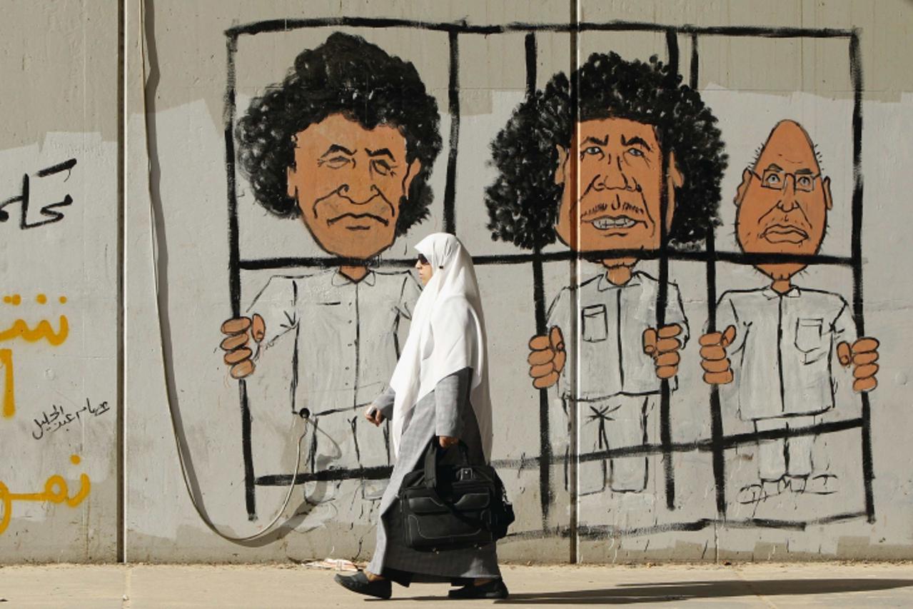 \'A woman walks past graffiti on a wall of former Libyan leader Muammar Gaddafi (C), his son Saif al-Islam Gaddafi (R) and former head of the Libyan Intelligence Service Abdullah Al-Senussi in Tripoli