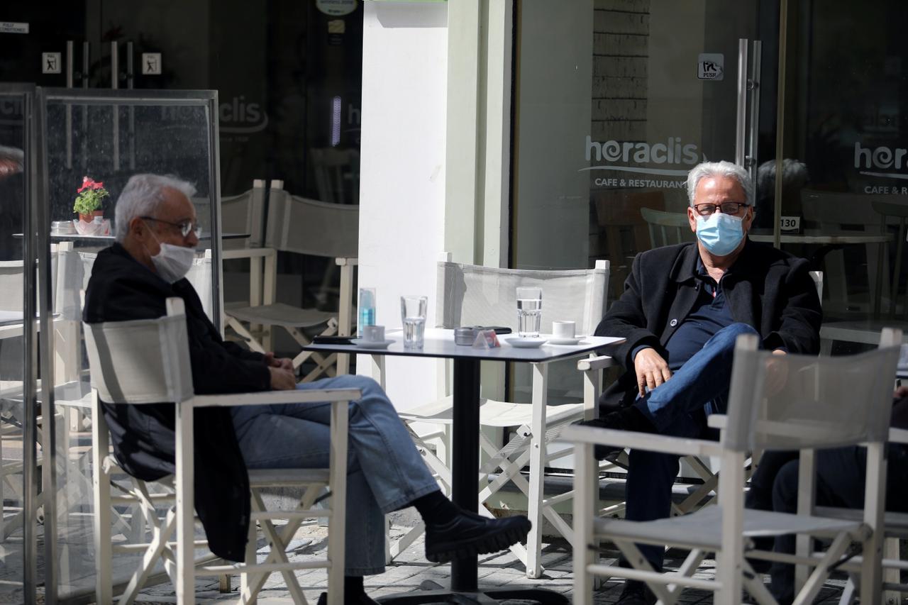 People, wearing protective masks, sit in a cafe in Nicosia