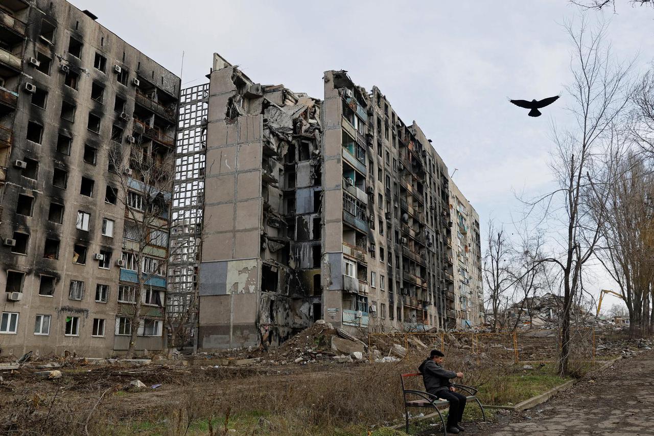 A local resident sits in front of destroyed apartment blocks in Mariupol