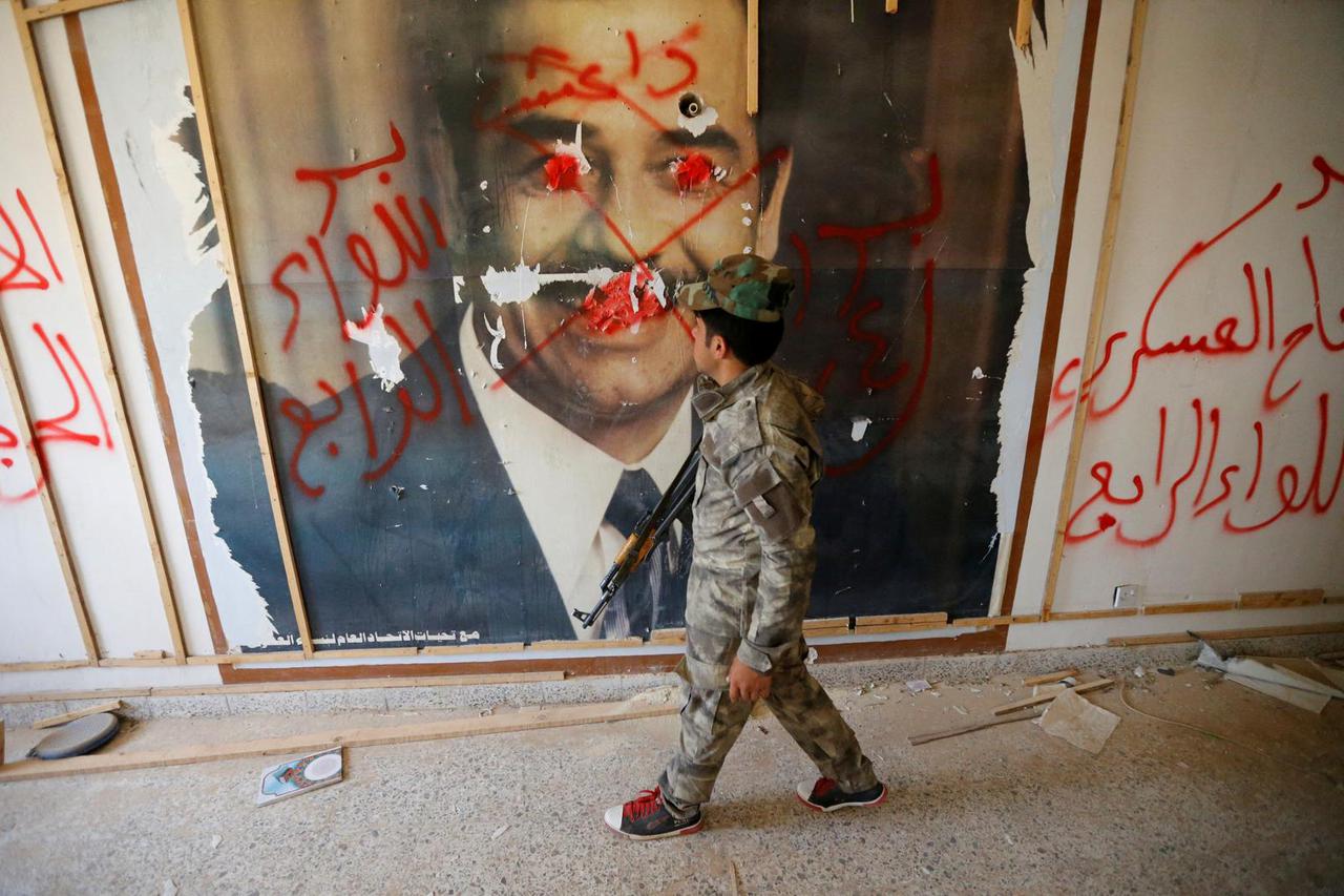 FILE PHOTO: A fighter from the Iraqi Shi'ite Badr Organization looks at a poster depicting images of former Iraqi President Saddam Hussein on the outskirts of Falluja