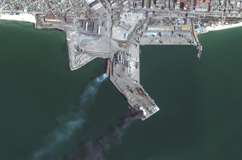 A satellite image shows a burned and partially submerged Russian Alligator-class landing ship and smoke rising nearby, in Berdiansk