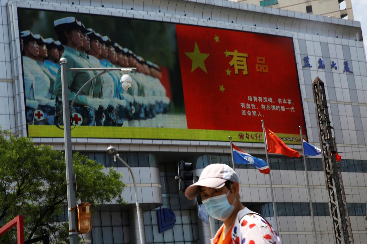 Pedestrian wearing a face mask walks past a screen showing an image of Chinese People's Liberation Army (PLA) soldiers next to a Chinese national flag, on the day of the opening session of the National People's Congress (NPC), in Beijing