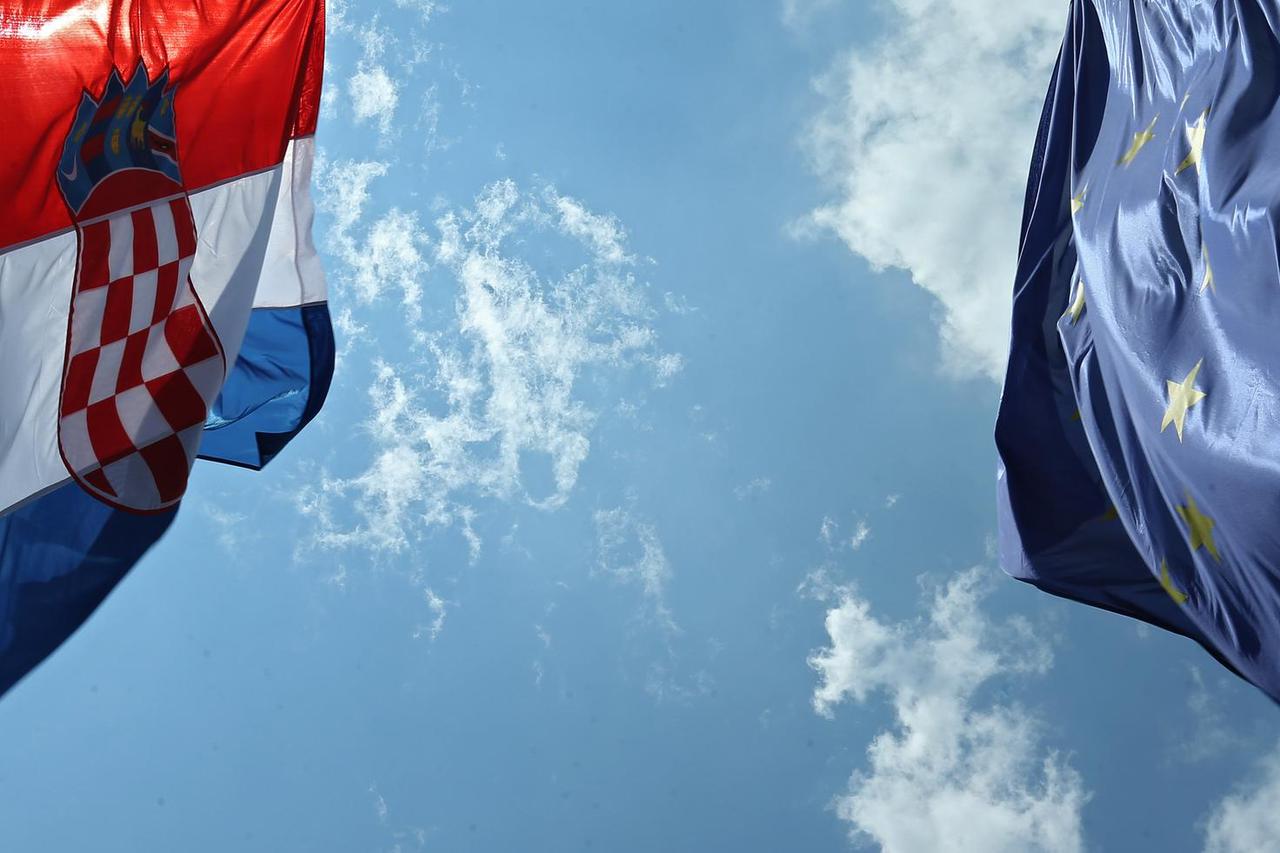 Zastave Hrvatske i Europske unije podignute prema vedrom nebu i suncu