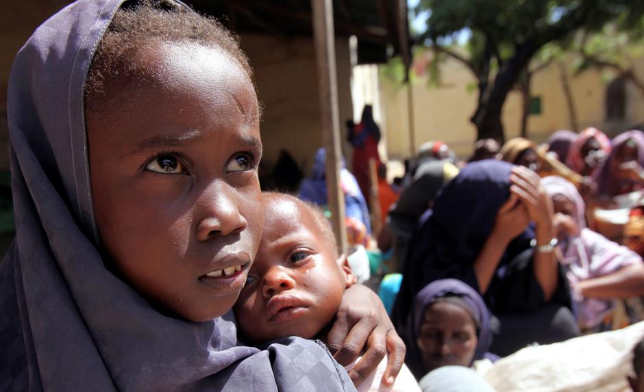 FILE PHOTO: Internally displaced Somali girl carries her sibling as they wait to collect food relief from the WFP at a settlement in the capital Mogadishu