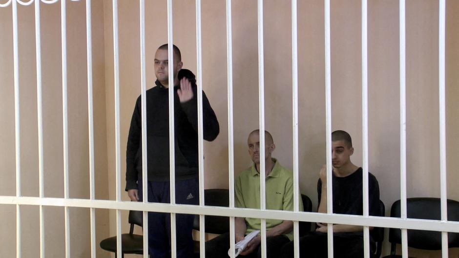 FILE PHOTO: A still image shows Britons Aiden Aslin, Shaun Pinner and Moroccan Brahim Saadoun in a courtroom cage at a location given as Donetsk
