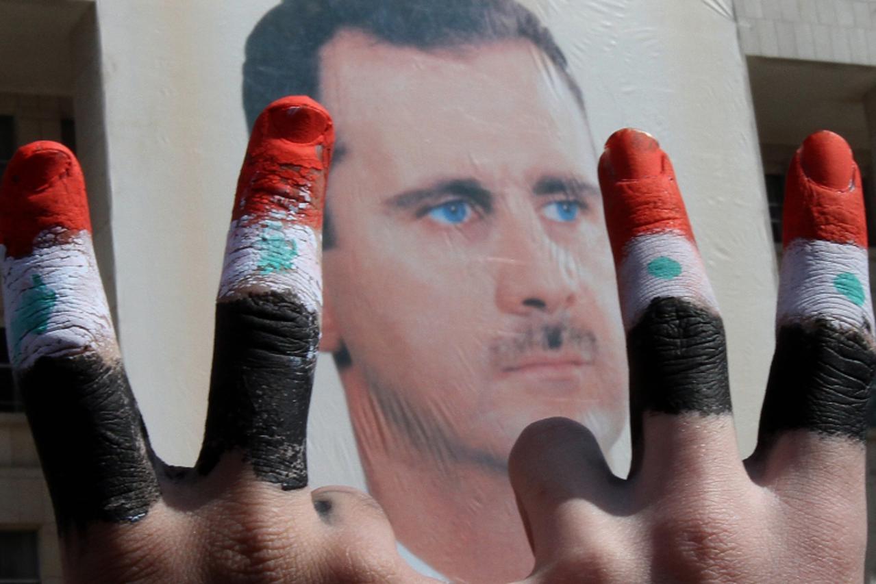 'Two men with the fingers painted in the colours of the Syrian flag show the V-sign as they pose in front of a huge image of President Bashar al-Assad during a rally by thousands supporters for their 