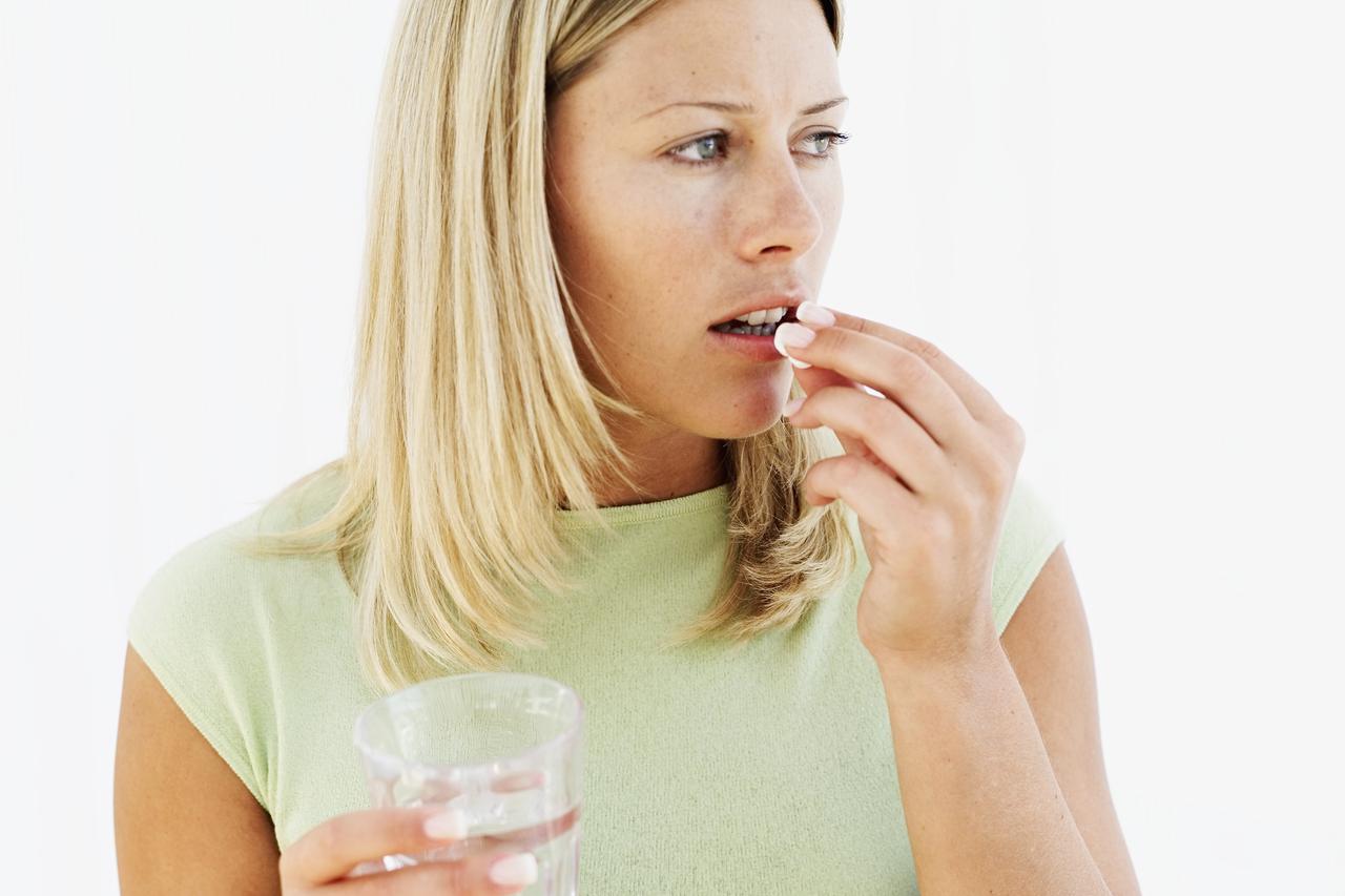 young woman holding a glass of water and taking a pill