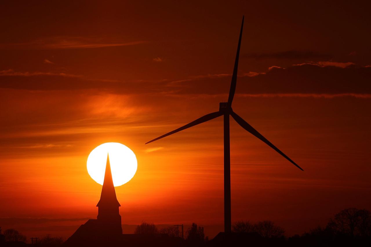 A power-generating windmill turbine and a church are pictured during sunset at a wind park in Ecoust-Saint-Mein