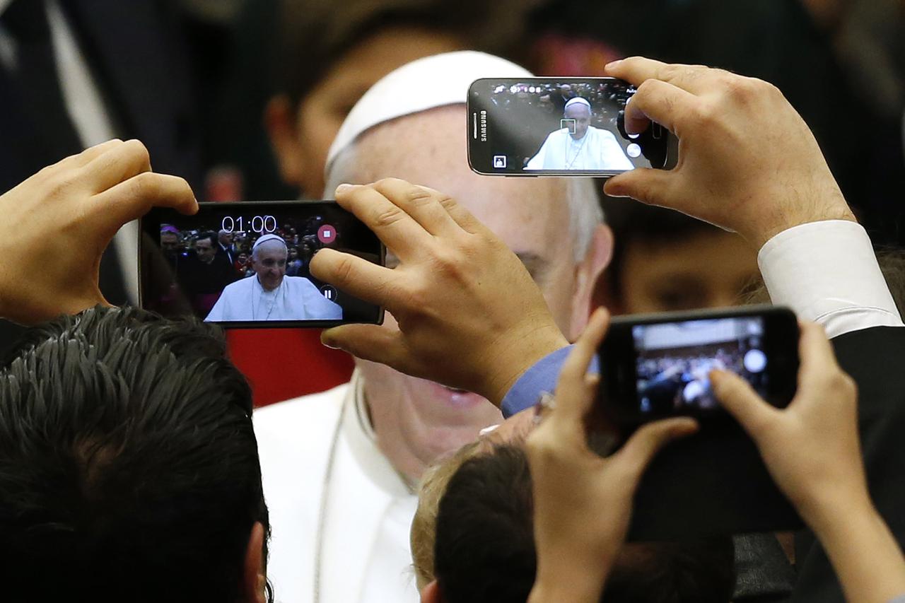 Pope Francis is pictured by mobile phones as he arrives to lead a special audience for Vatican employees and their families at the Paul VI's hall at the Vatican December 22, 2014.  REUTERS/Alessandro Bianchi (VATICAN - Tags: RELIGION TPX IMAGES OF THE DAY